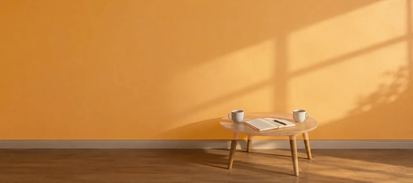 Enquête métier : une table basse avec un carnet ouvert, un stylo et deux tasses de café, contre un mur doré éclairé par la lumière d'une fenêtre