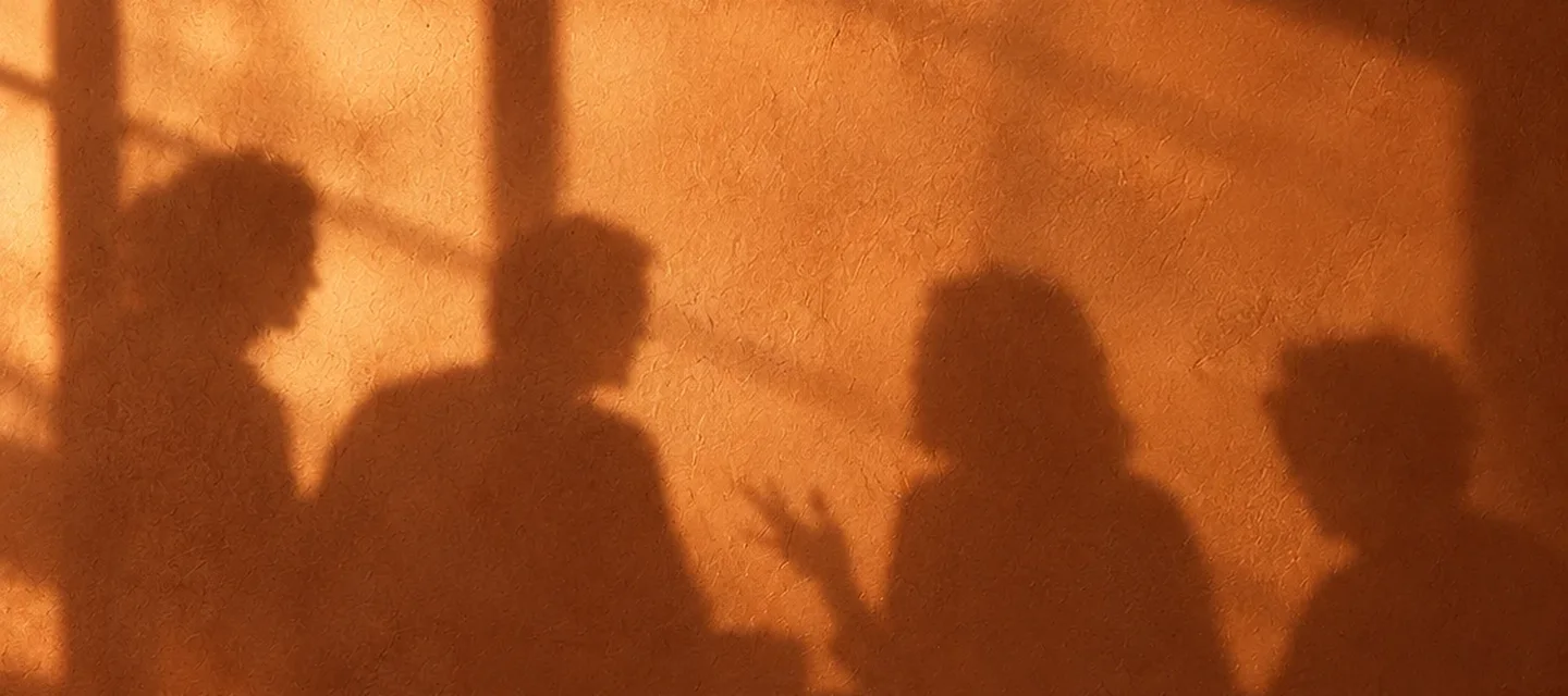 YUMANconnect : un parcours chaque mois pour avancer ensemble Ombres de quatre personnes en pleine conversation sur un mur terracotta, dans la lumière d'une fenêtre